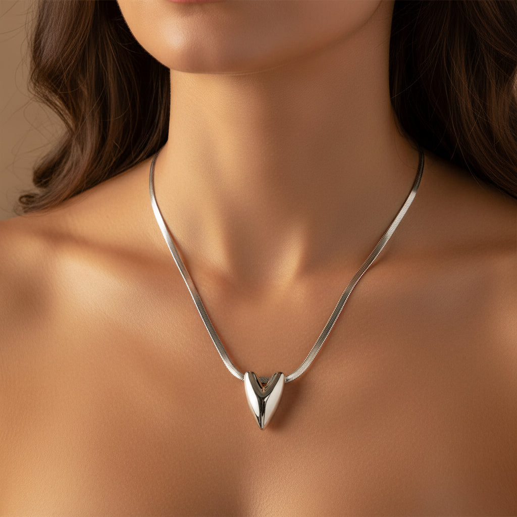 Silver heart-shaped pendant on a snake chain necklace against a white background